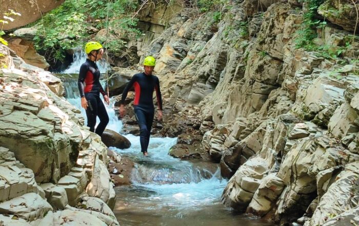 Due persone percorrono il torrente bagnone per una attività di River Trekking, con muta, caschetto e giubbotto salvagente.