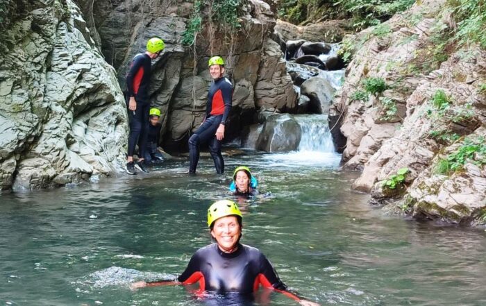 Alcune persone scendono lungo il torrente Bagnone con muta, caschetto e giubbotto salvagente per una attività di river trekking.